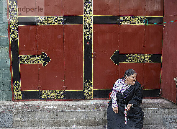 Tibetische Frau sitzt auf den Stufen vor einer roten Tür; Lhasa  Tibet