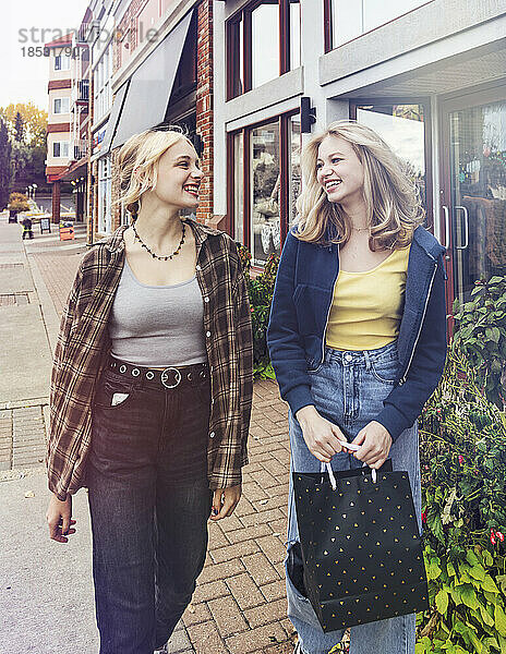 Zwei Teenager genießen einen gemeinsamen Tag beim Einkaufen und gehen an einem Herbsttag eine Straße entlang; St. Albert  Alberta  Kanada