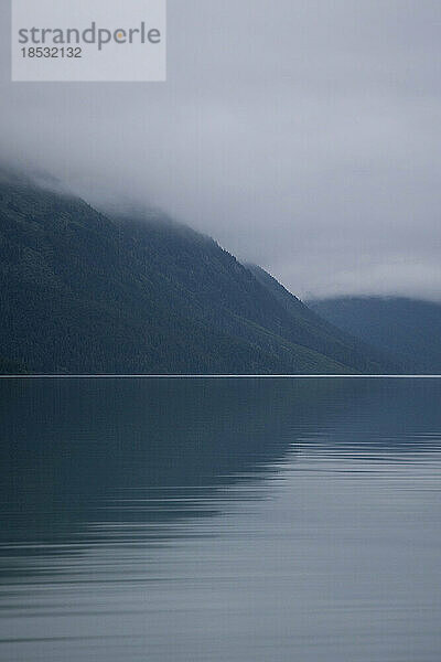 Stimmungsvolle Reflexionen auf dem ruhigen Wasser des Kenai Lake an einem nebligen Tag im Chugach National Forest auf der Kenai-Halbinsel; Cooper Landing  Alaska  Vereinigte Staaten von Amerika
