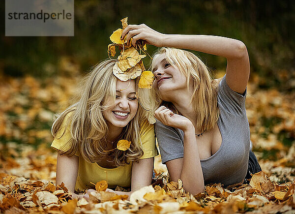 Zwei Mädchen im Teenageralter liegen im Laub und haben Spaß in einem Stadtpark an einem warmen Herbstnachmittag; St. Albert  Alberta  Kanada.