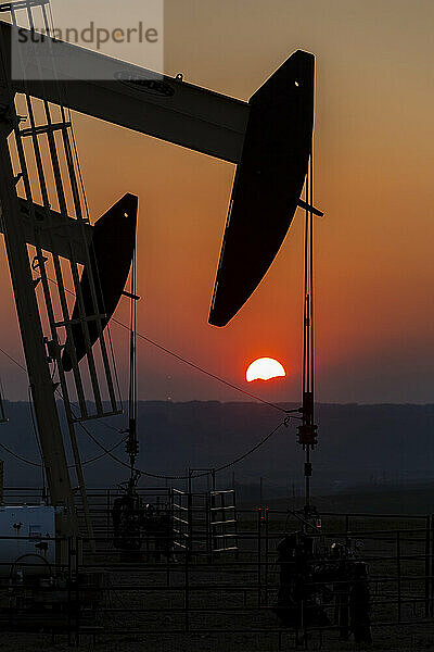 Silhouette von Pumpjacks mit einem orange leuchtenden Himmel bei Sonnenuntergang  westlich von Airdrie; Alberta  Kanada