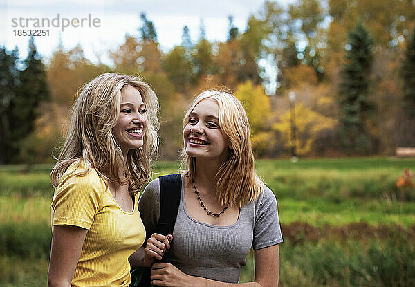 Zwei Mädchen im Teenageralter gehen an einem warmen Herbsttag zusammen in einem Stadtpark spazieren; St. Albert  Alberta  Kanada.