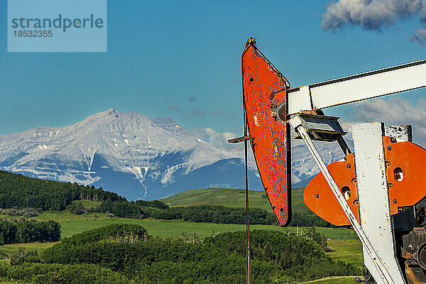 Nahaufnahme eines Pumpjack-Kopfes mit sanften grünen Hügeln  Bergkette  blauem Himmel und Wolken im Hintergrund  nördlich von Longview  Alberta; Alberta  Kanada