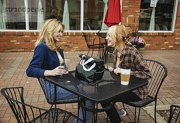 Zwei Teenager genießen die gemeinsame Zeit und sitzen nach dem Einkaufen in einem Café im Freien an einem Tisch und trinken Kaffee; St. Albert  Alberta  Kanada