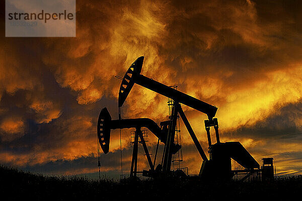 Silhouette von zwei Pumpjacks bei Sonnenaufgang mit dramatischen bunt leuchtenden Wolken im Hintergrund  westlich von Airdrie; Alberta  Kanada