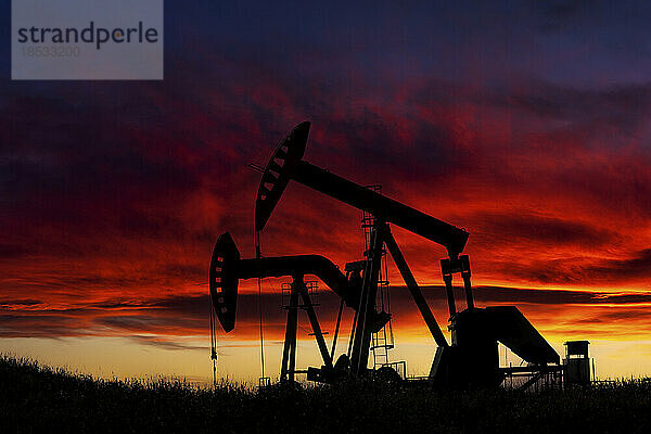 Silhouette von zwei Pumpjacks bei Sonnenaufgang mit einer dramatischen bunten leuchtenden Wolken im Hintergrund  westlich von Airdrie; Alberta  Kanada