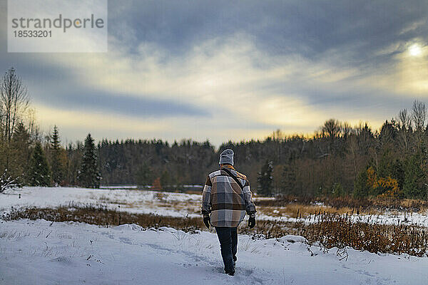 Junger Mann geht über ein verschneites Feld auf dem Lande; Surrey  British Columbia  Kanada