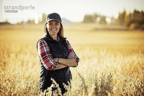 Porträt einer reifen Bäuerin in einem Getreidefeld  die während der Ernte bei Sonnenuntergang für die Kamera posiert; Alcomdale  Alberta  Kanada