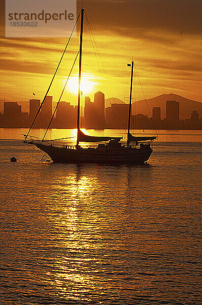 Silhouette eines Segelboots bei Sonnenaufgang mit der Skyline von San Diego in der Ferne  Kalifornien  USA; San Diego  Kalifornien  Vereinigte Staaten von Amerika