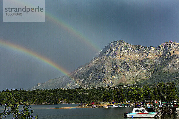 Doppelter Regenbogen mit Berg entlang eines Seeufers und dunkelblauem Himmel im Waterton Lakes National Park; Waterton  Alberta  Kanada