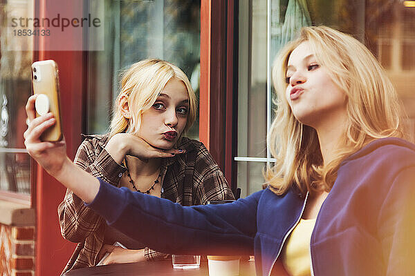Zwei Teenager genießen die gemeinsame Zeit in einem Café im Freien und verbringen Zeit mit ihren Smartphones  um Selbstporträts zu machen; St. Albert  Alberta  Kanada