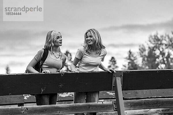 Schwarz-Weiß-Bild von zwei Mädchen im Teenageralter  die auf einer Brücke stehen und Zeit miteinander in einem Stadtpark verbringen; St. Albert  Alberta  Kanada.