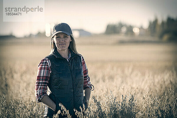 Nahaufnahme einer reifen Bäuerin in einem Getreidefeld  die während der Ernte bei Sonnenuntergang für die Kamera posiert; Alcomdale  Alberta  Kanada