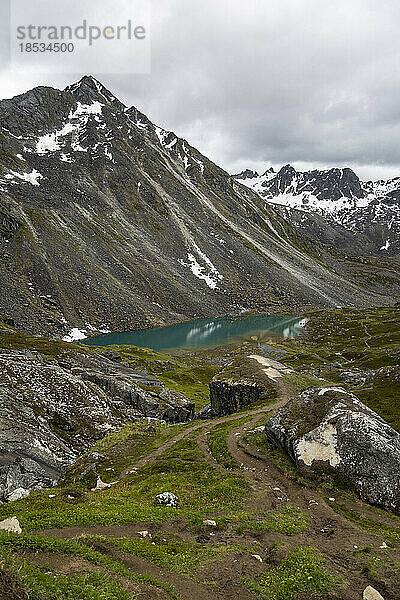 Granitgipfel am Hatcher Pass unter grauem  bewölktem Himmel mit dem dunkel türkisfarbenen Wasser der Reed Lakes in der Nähe der Independence Mine; Palmer  Alaska  Vereinigte Staaten von Amerika