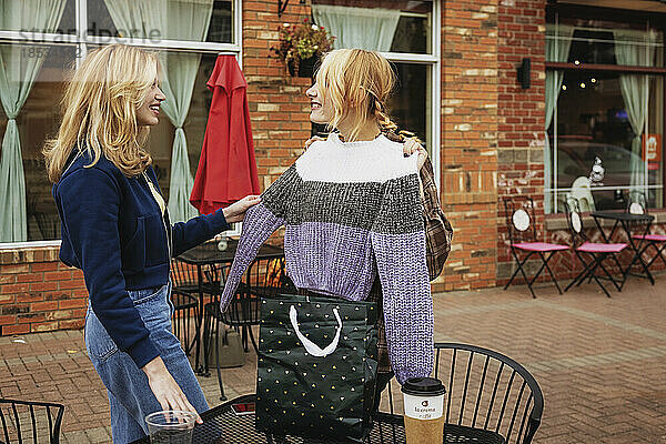 Zwei Teenager genießen die gemeinsame Zeit in einem Straßencafé  als ein Freund den anderen mit einem Pullover überrascht; St. Albert  Alberta  Kanada