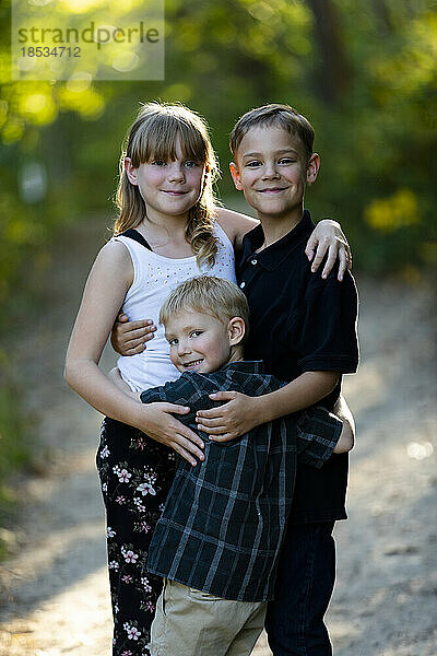 Außenporträt von drei jungen Geschwistern  einer Schwester und zwei Brüdern  auf einem Parkweg; Edmonton  Alberta  Kanada