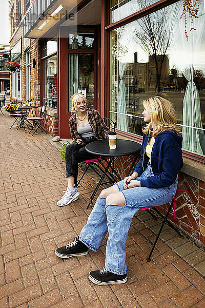 Zwei Teenager genießen die gemeinsame Zeit und sitzen an einem Kaffeetisch in einem Straßencafé; St. Albert  Alberta  Kanada