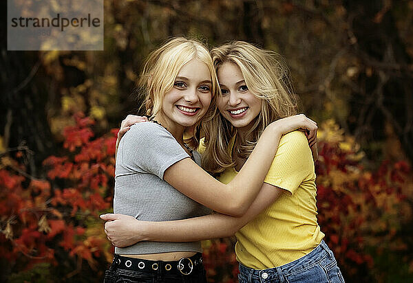 Porträt von zwei Mädchen im Teenageralter  die an einem warmen Herbstnachmittag in einem Stadtpark für die Kamera posieren; St. Albert  Alberta  Kanada.