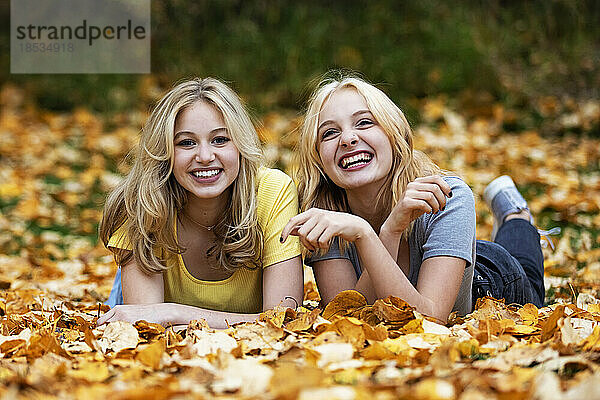Porträt von zwei Mädchen im Teenageralter  die in einem Stadtpark an einem warmen Herbstnachmittag im Laub liegen und für die Kamera posieren; St. Albert  Alberta  Kanada.
