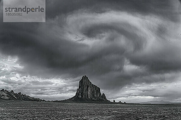 Wolken  die wie ein Wirbel über Shiprock in der Hochwüstenebene der Navajo Nation in New Mexico  USA  aussehen  bearbeitet in Schwarz-Weiß; Shiprock  New Mexico  Vereinigte Staaten von Amerika