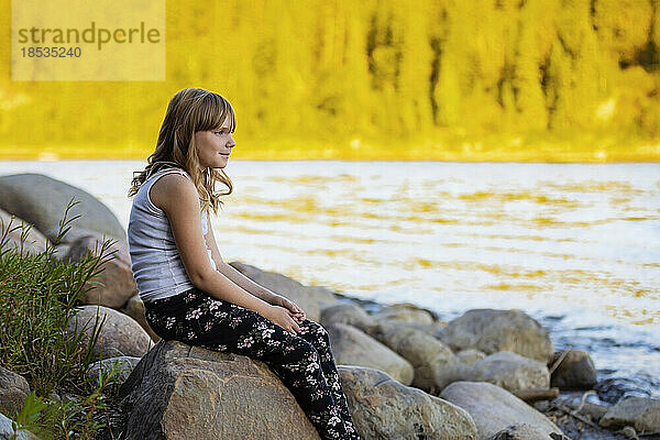 Porträt eines Mädchens im Freien  das im Herbst an einem Wasser sitzt; Edmonton  Alberta  Kanada