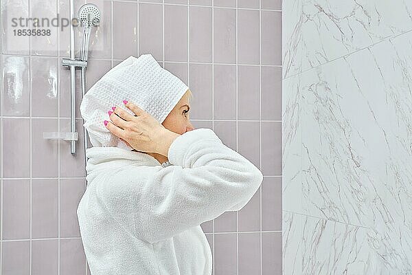 Frau mittleren Alters im Bademantel wickelt ihr Haar nach der Dusche in ein Handtuch