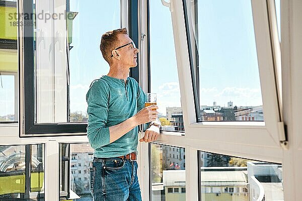 Mann mittleren Alters mit Brille steht auf dem Balkon eines Hochhauses