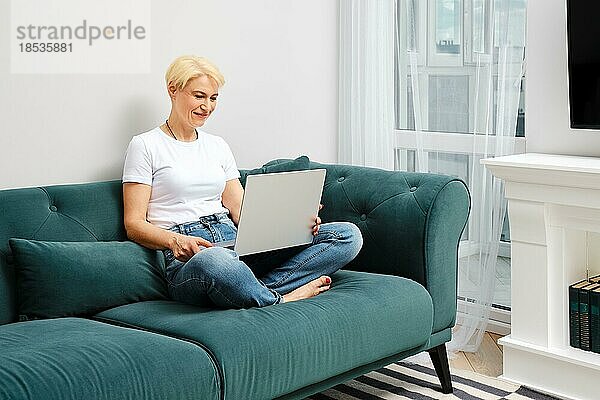 Eine Frau mittleren Alters chattet online mit einer Freundin in ihrer neuen Wohnung. Konzept des cleveren Alterns und der Anpassung an die neue Realität