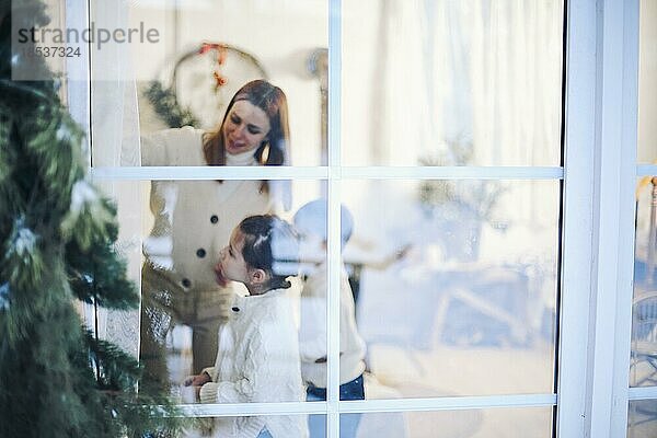 Weihnachtszeit. Porträt der Familie mit zwei kleinen Kindern versammelt am Fenster zu Hause schmücken Weihnachtsbaum zusammen  glückliche Eltern und Kinder in Erwartung der Ankunft der Winterferien  selektiver Fokus