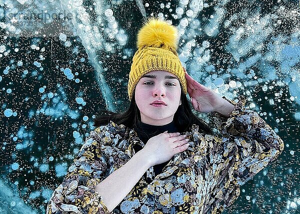 Modisches Bild einer atemberaubenden Frau  die auf dem Eis des Baikalsees posiert und einen gelben Hut trägt. Boho Kleid fliegt im Wind. Schöne Eislandschaften des Baikalsees
