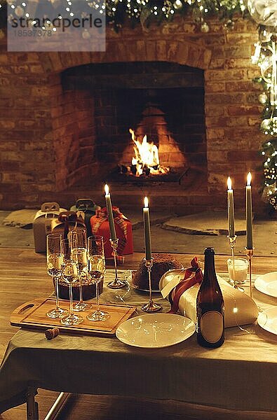 Weihnachten oder Neujahr Abendessen gegen brennenden Kamin und Weihnachtsgeschenke in gemütlichen Haus mit LEDlichter festlichen Tisch mit frisch gebackenen Kuchen  Kerzen  Gläser Champagner  selektiven Fokus dekoriert