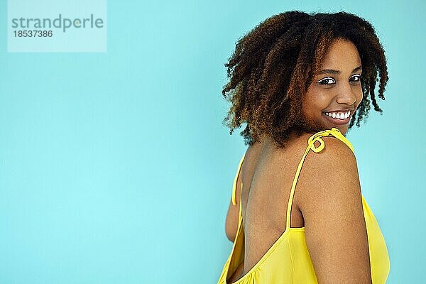 Schöne helle freudige afrikanische Frau in gelbem Kleid in blauem Studio Hintergrund