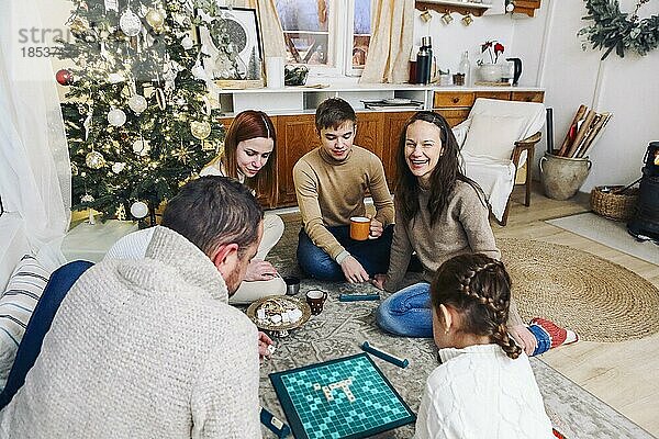 Große Familie sitzt auf dem Boden und spielt gemeinsam intellektuelle Brettspiele  während sie ihre Freizeit zu Hause verbringen. Vater  Mutter  Großmutter und Kinder spielen traditionelles Spiel mit Buchstabenfliesen