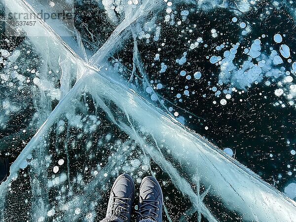 Brüchiges  dünnes  sprödes Eis unter den Füssen Weibliche Füße auf Eis. Frau trägt Winterschuhe auf dem Eis des Baikalsees  Russland. Risse auf Eis Hintergrund. Eis des Baikalsees. Urlaub und Reise Konzept