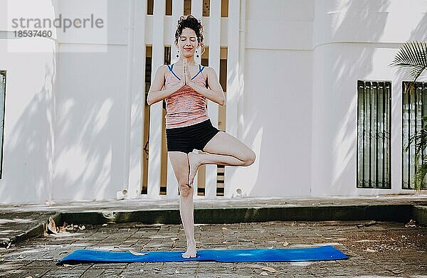 Mädchen macht Yoga Vrikshasana oder Baum Pose im Freien. Junge Frau macht Vrikshasana Yoga im Freien. Entspannung und Vitalität Yogakonzept