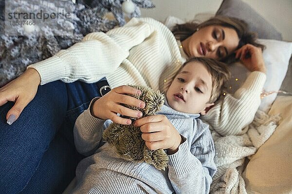 Gemütliche Weihnachten Porträt der jungen Familie Mutter und kleiner Sohn lächelnd in die Kamera beim Entspannen zusammen auf dem Sofa in der Nähe von Weihnachtsbaum zu Hause  Mutter und Kind genießen Winterferien zusammen. Blick von oben