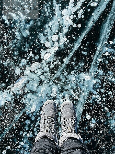 Brüchiges  dünnes  sprödes Eis unter den Füssen Weibliche Füße auf Eis. Frau trägt Winterschuhe auf dem Eis des Baikalsees  Russland. Risse auf Eis Hintergrund. Eis des Baikalsees. Urlaub und Reise Konzept