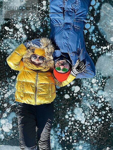 Glückliches Paar auf dem zugefrorenen Baikalsee in Winterkleidung. Transparentes Eis. Reisen im Winter  aktive Erholung  Sport  Urlaub