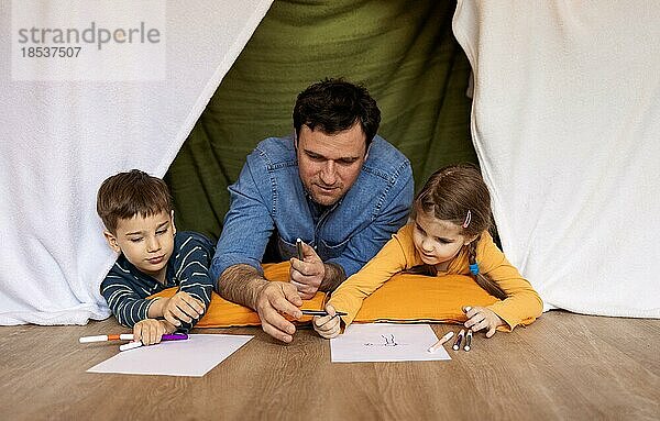 Glücklicher Vater mit kleiner Tochter und Sohn Zeichnung drinnen in handgemachten Wigwam. Familie  Spaß und Hobby Konzept