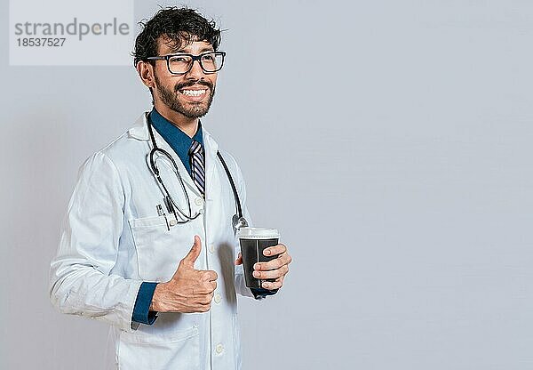 Junger Arzt hält einen Kaffee zum Mitnehmen isoliert. Lächelnder Arzt hält Kaffee mit Daumen nach oben  Zufriedener Arzt hält Kaffee zum Mitnehmen isoliert