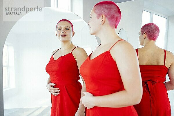 Schöne entspannte Frau in rotem langen Kleid und roten Haaren schaut in den Spiegel. Konzept der Körper positiv