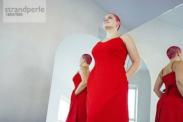 Schöne entspannte Frau in rotem langen Kleid und roten Haaren schaut in den Spiegel. Konzept der Körper positiv