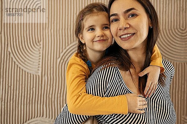 Mama und kleine Tochter umarmen auf beige Hintergrund mit Kopie Raum  glückliche Familie  Elternschaft. Konzept der mütterlichen Liebe und Fürsorge