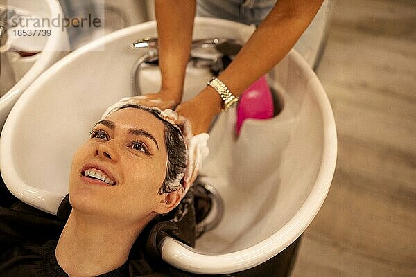 Fröhliche junge Brünette Frau genießt Kopfmassage und Haare waschen  während sie ihre Haarpflege