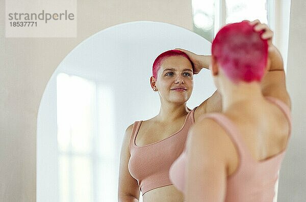 Schöne entspannte Frau in Sportkleidung roten Schuss Haar Blick in den Spiegel. Konzept der Körper positiv