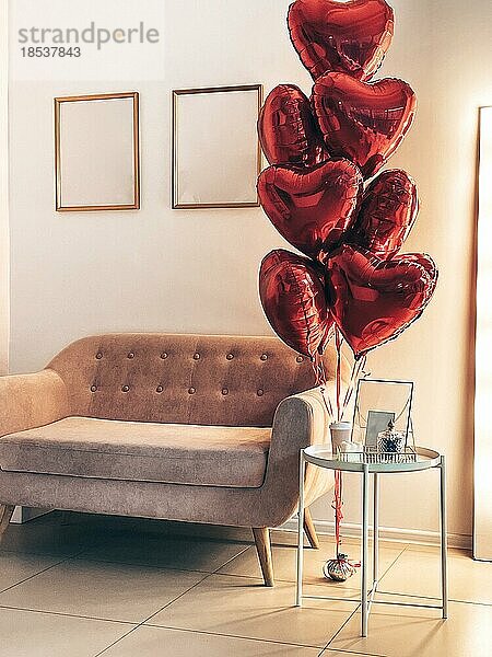 Interieur eines stilvollen Wohnzimmers  das für den Valentinstag dekoriert wurde. Geschenke und Kaffee auf dem Tisch und Herzen Luftballons in der Nähe des rosa Sofa