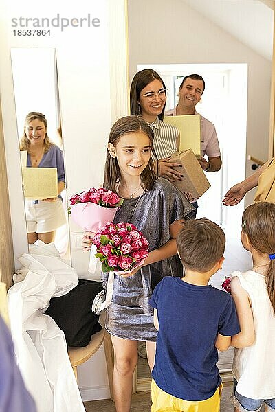 Glücklich lächelnde Gäste mit Geschenken stehen in der Tür. Fokus auf junge Frau. Glücklicher Hochzeitstag oder Jahrestag. Pepple mit fröhlichen Kindern