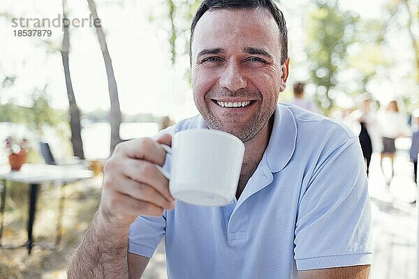 Glücklicher Mann  der an einem angenehmen Sommertag in einem Café im Freien am Strand eine leckere Kaffeepause macht