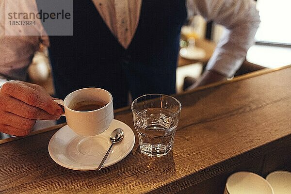Männliche Hand hält weiße Tasse mit Espresso. Nahaufnahme mit selektivem Fokus. Blick auf Espresso bei einem Geschäftstreffen