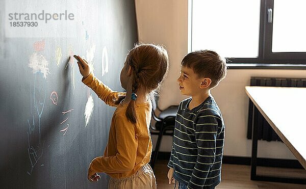 Nettes kleines Mädchen und Junge Zeichnung mit Buntstift Farbe an der Wand. Werke des Kindes. Niedliche Geschwister schreiben auf Kreidetafel